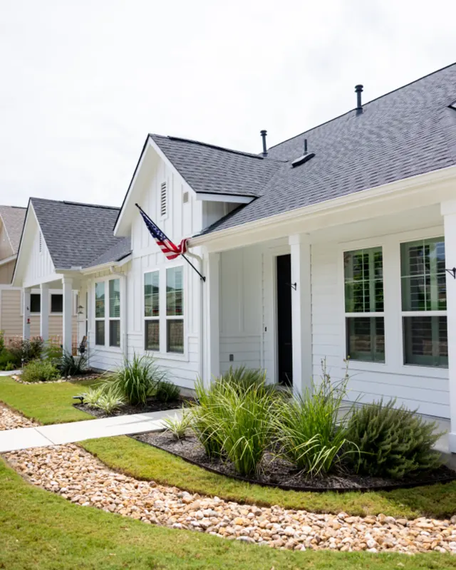 A white clapboard home in Elmira with trimmed ornamental grasses, a clean gravel border and a freshly cut lawn.